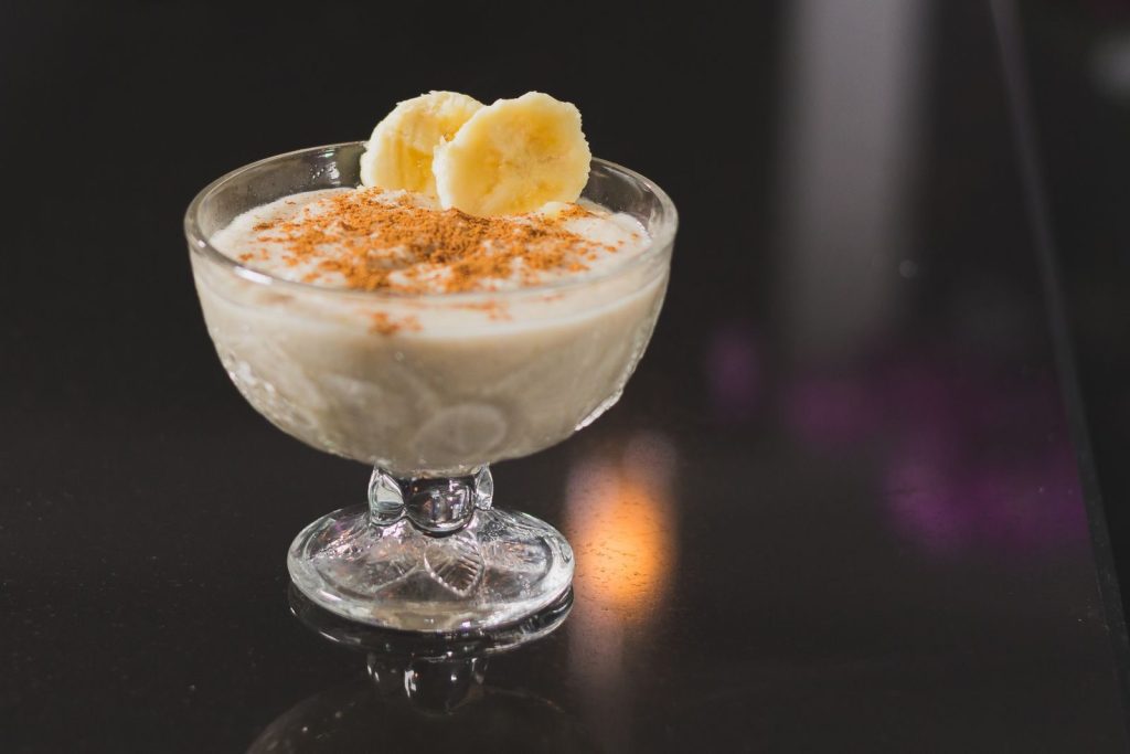 Creamy banana dessert topped with cinnamon served in a stemware on a reflective surface.