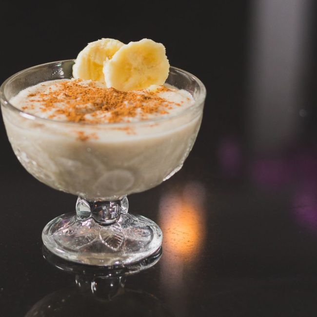 Creamy banana dessert topped with cinnamon served in a stemware on a reflective surface.