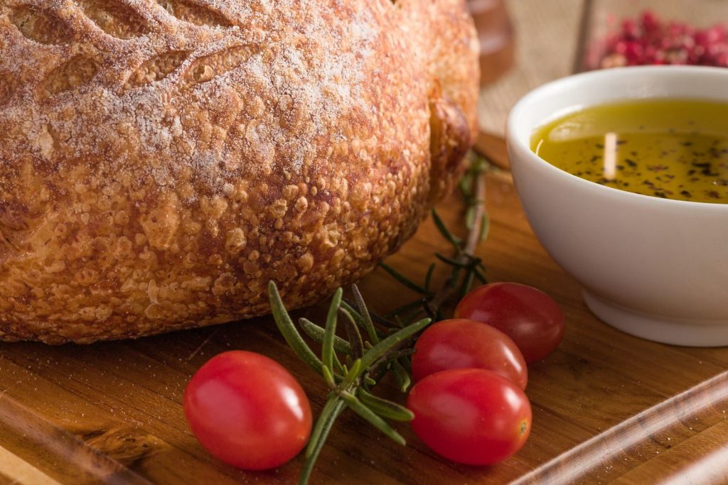 Close-up of artisan bread with olive oil dip and cherry tomatoes on a wooden board.